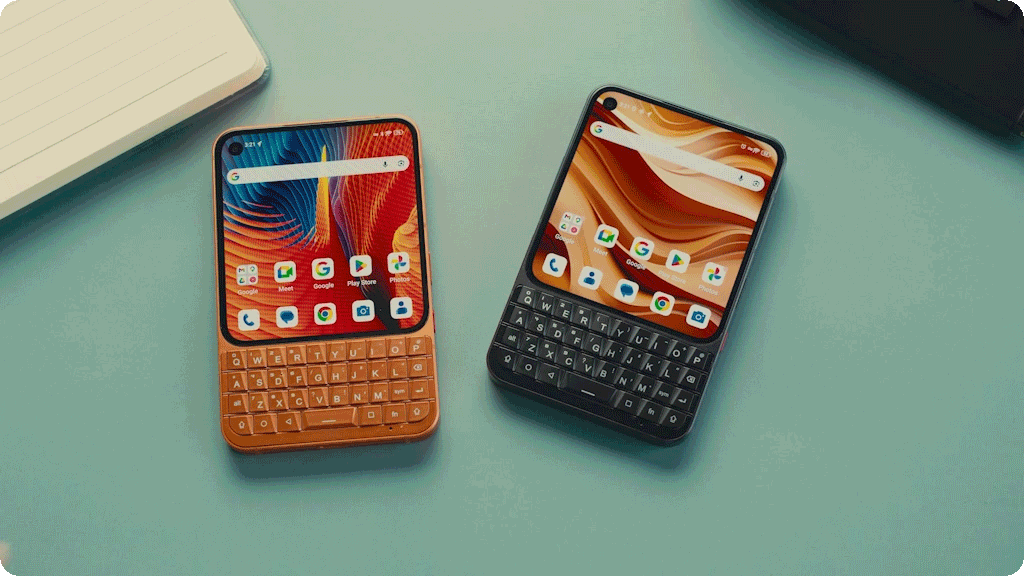 An orange and a black Unihertz Titan 2 Elite smartphone are displayed side-by-side on a blue surface, showcasing their physical QWERTY keyboards and Android home screens.