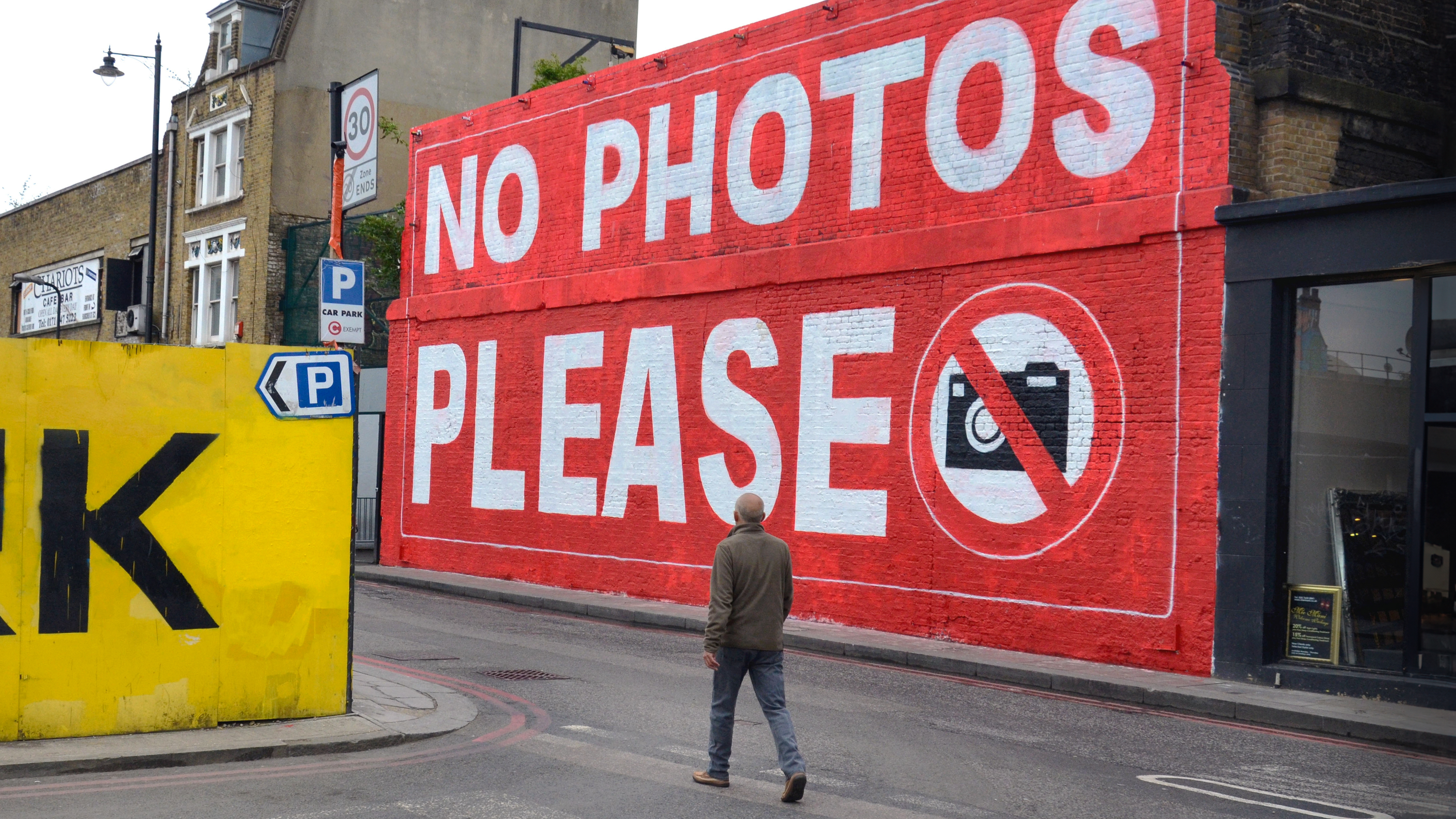 D90R8B A man walking by a large No Photos Please sign on the wall of Village Underground in Holywell Lane, Shoreditch, London.